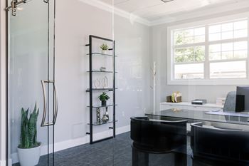 A black piano sits in front of a glass wall in a bright room.